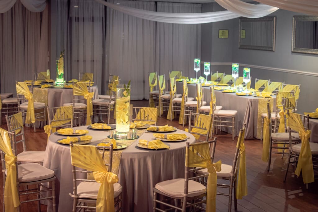 wedding reception decor with round tables and chairs with yellow sashes